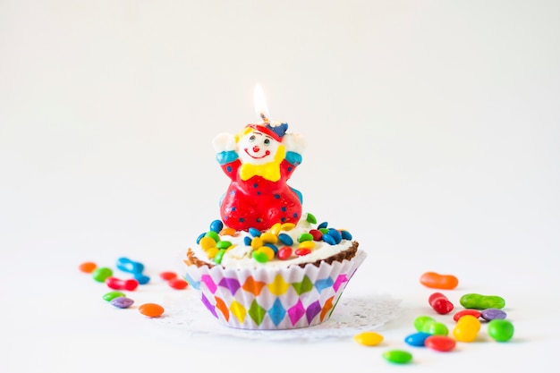 Torta decorativa de la taza con la vela iluminada del payaso en el fondo blanco