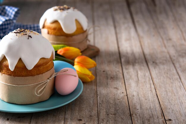 Torta tradicional de Pascua, huevos coloridos y tulipanes en mesa de madera.