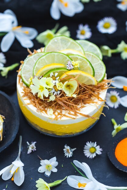 Torta vegana cruda con limón y lima sobre una superficie negra cubierta con diminutas flores de margarita