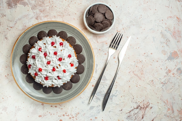 Torta de vista inferior con crema pastelera en placa ovalada chocolate en un tazón tenedor y cuchillo de cena en mesa beige