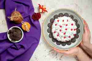 Foto gratuita torta de vista superior con crema pastelera blanca en placa en galletas de mano de mujer atadas con tazón de chocolate de cuerda en shaw púrpura