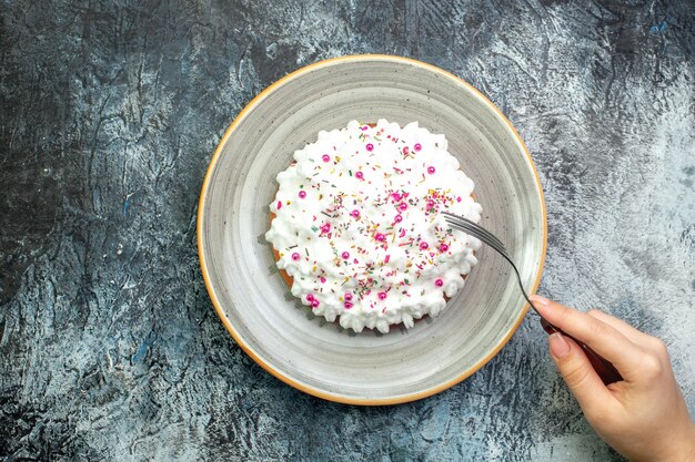 Torta de vista superior con crema pastelera blanca en tenedor de plato redondo gris en mano femenina en mesa gris