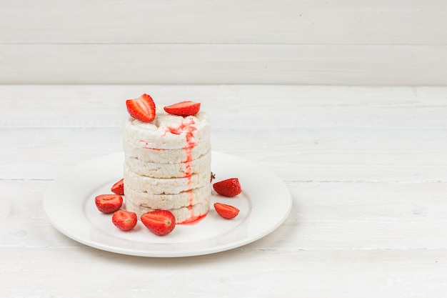 Tortas de arroz blanco de vista de ángulo alto en un plato con fresas en la superficie de la placa de madera blanca.