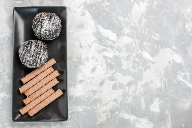 Tortas de chocolate de vista superior con galletas de pipa dulce dentro de la placa negra en el escritorio blanco