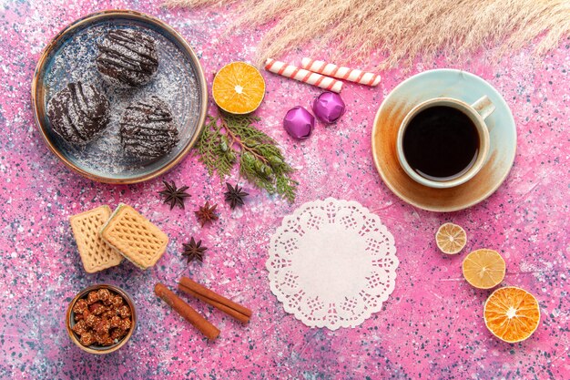 Tortas de chocolate de vista superior con waffles y taza de té en el escritorio rosa