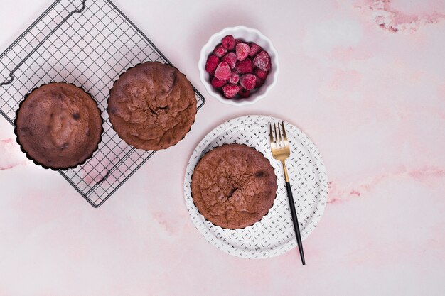 Tortas horneadas caseras en una bandeja para hornear y platos con un tazón de frambuesas congeladas sobre fondo rosa