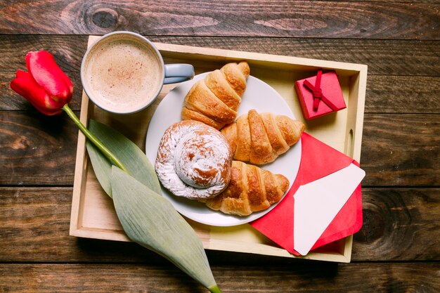 Tortas en el plato cerca de la flor, taza de bebida, carta y caja de regalo a bordo