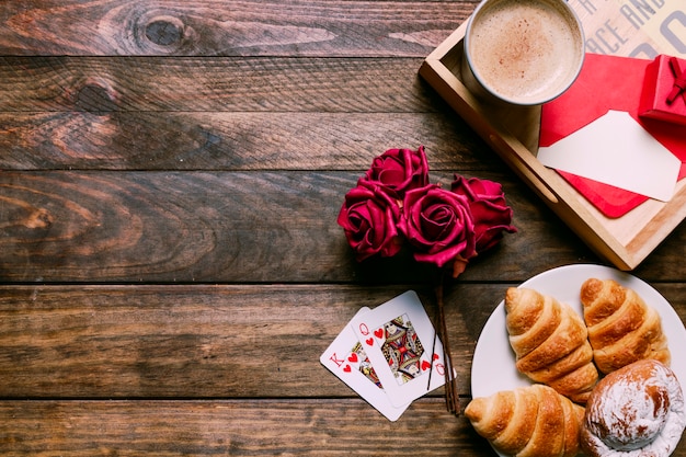 Tortas en el plato cerca de las flores y jugando a las cartas cerca de la taza de bebida y carta a bordo