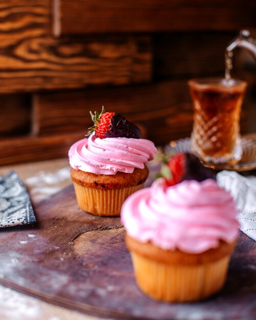 Tortas de vista frontal con crema rosa y fresa junto con té caliente en la superficie marrón