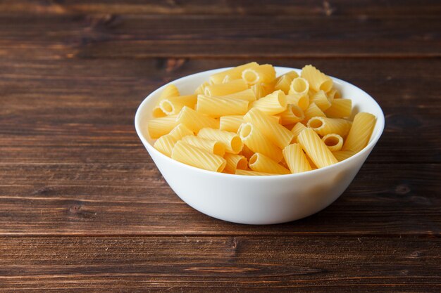 Tortiglioni pasta en un recipiente sobre una mesa de madera. Vista de ángulo alto.