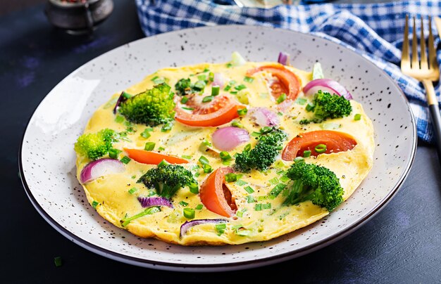 Tortilla con brócoli, tomates y cebollas rojas sobre mesa oscura. Frittata italiana con verduras.