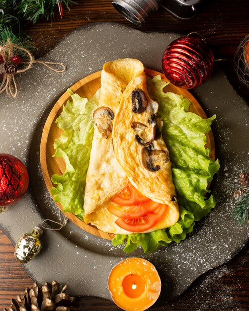 Tortilla de champiñones colocada sobre lechuga y envuelta alrededor de rodajas de tomate