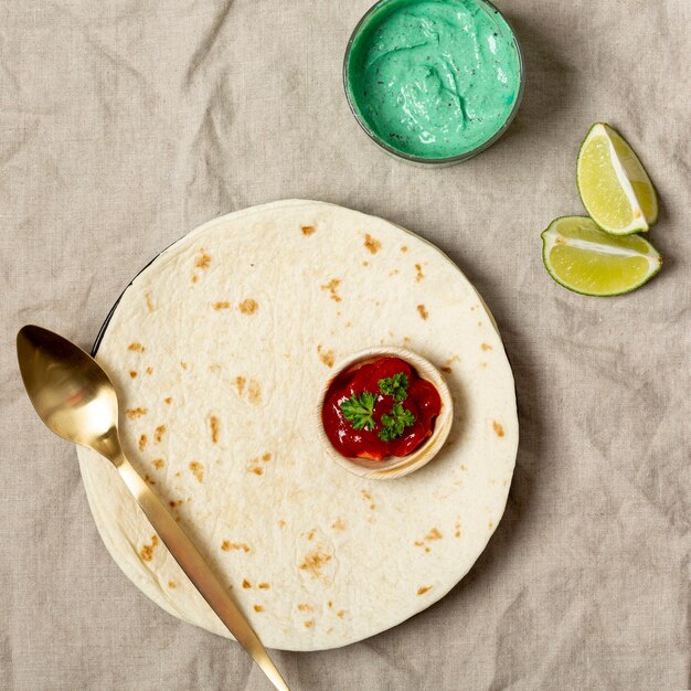 Tortilla con cuchara y varias salsas cerca de rodajas de lima