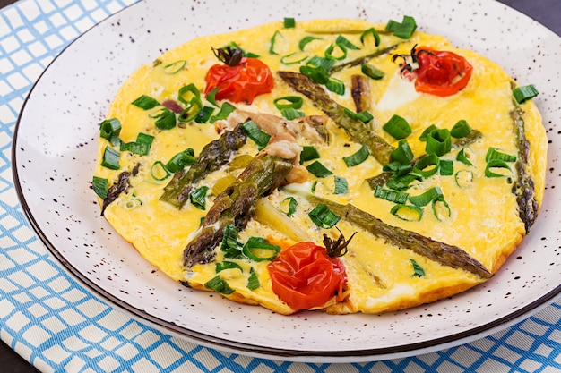 Tortilla con espárragos y tomate para el desayuno en una mesa de madera.