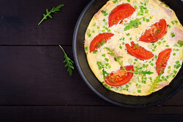 Tortilla con tomate, jamón y cebolla verde en mesa oscura