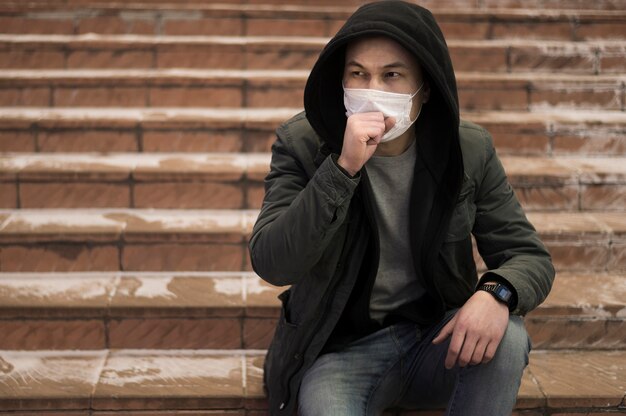 Tos hombre posando en las escaleras mientras usa máscara médica