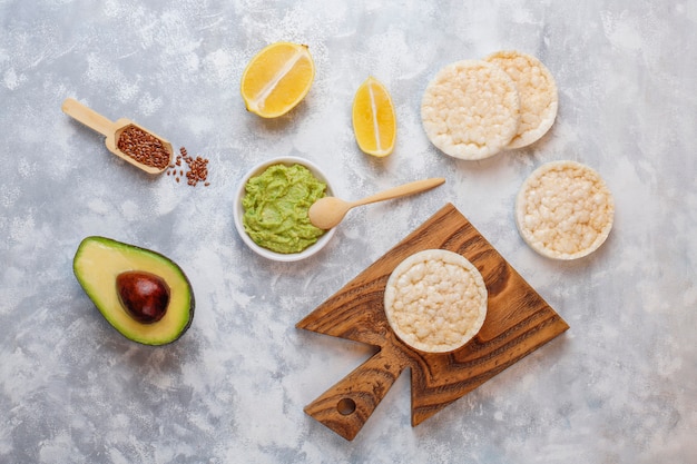 Tostada abierta de aguacate con pan de arroz, rodaja de limón, rodajas de aguacate, vista superior de semillas.