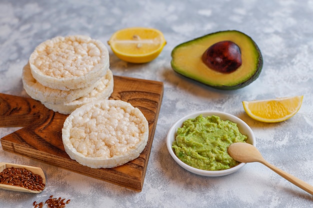 Tostada abierta de aguacate con pan de arroz, rodaja de limón, rodajas de aguacate, vista superior de semillas.