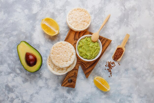 Tostada abierta de aguacate con pan de arroz, rodaja de limón, rodajas de aguacate, vista superior de semillas.