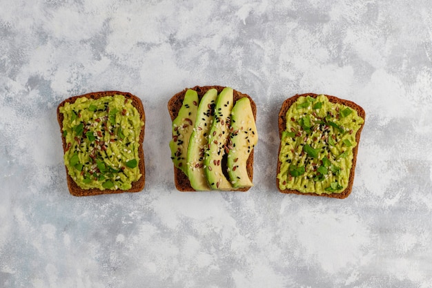 Tostada abierta de aguacate con rodajas de aguacate, limón, semillas de lino, semillas de sésamo, rebanadas de pan negro, vista superior