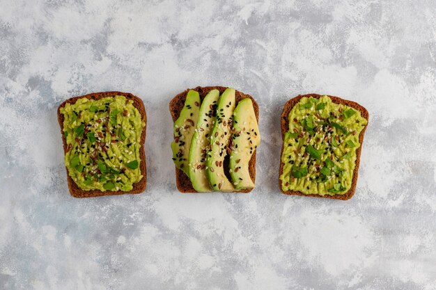 Tostada abierta de aguacate con rodajas de aguacate, limón, semillas de lino, semillas de sésamo, rebanadas de pan negro, vista superior