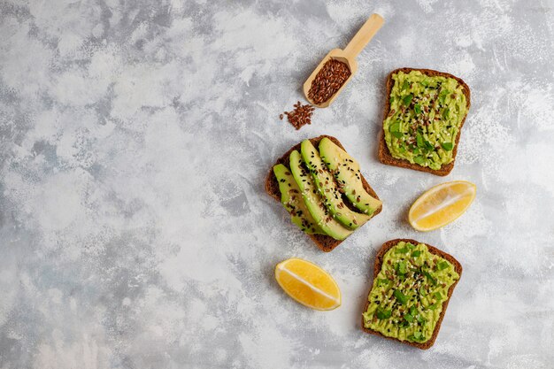 Tostada abierta de aguacate con rodajas de aguacate, limón, semillas de lino, semillas de sésamo, rebanadas de pan negro, vista superior