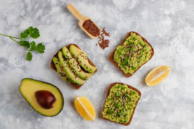 Tostada abierta de aguacate con rodajas de aguacate, limón, semillas de lino, semillas de sésamo, rebanadas de pan negro, vista superior