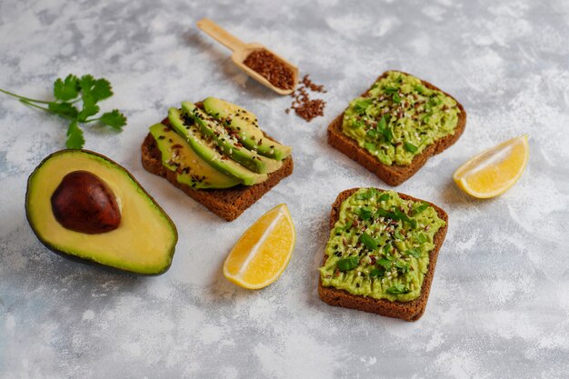 Tostada abierta de aguacate con rodajas de aguacate, limón, semillas de lino, semillas de sésamo, rebanadas de pan negro, vista superior