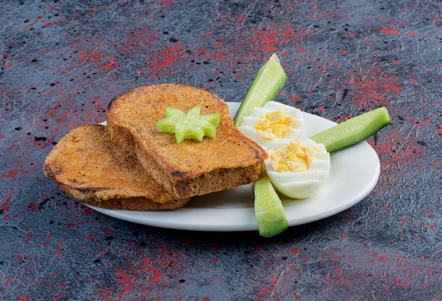 Tostada de pan con huevo cocido y pepinos.