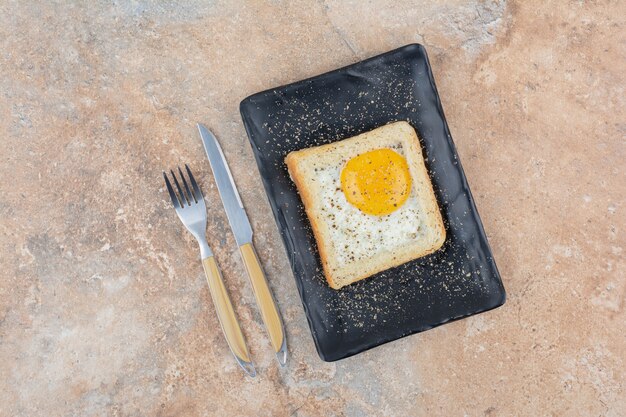 Tostadas de huevo con especias en placa negra con cubiertos