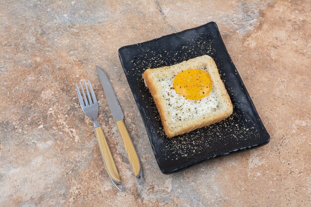 Tostadas de huevo con especias en placa negra con cubiertos