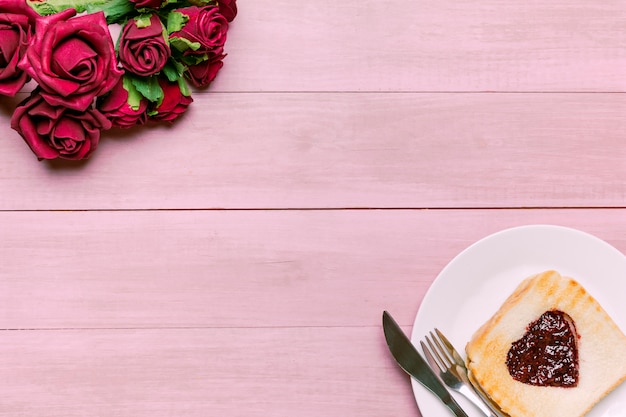 Tostadas con mermelada en forma de corazón con rosas rojas.