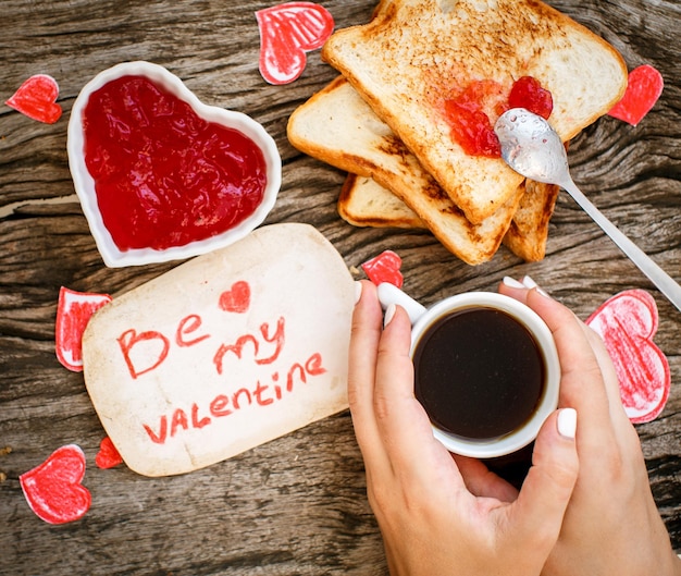 Tostadas con mermelada de fresa Tarjeta de mensaje blanca Be My Valentine con café en las manos Día de San Valentín