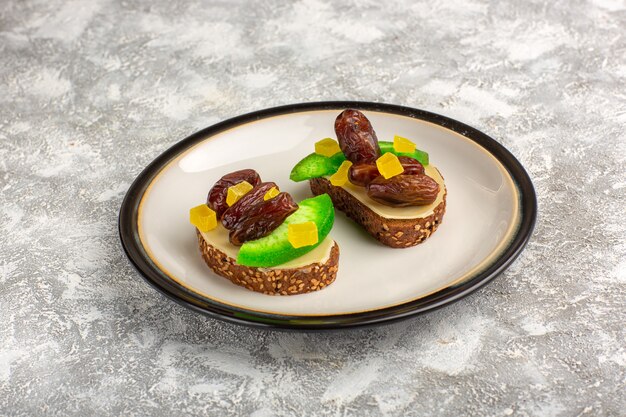 Tostadas de pan de vista frontal con pepino y ciruelas secas dentro de la placa sobre la superficie blanca