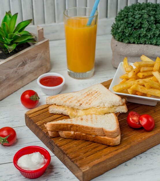 Tostadas de sándwich con queso dentro con papas fritas, salsa de tomate y un vaso de jugo de naranja.