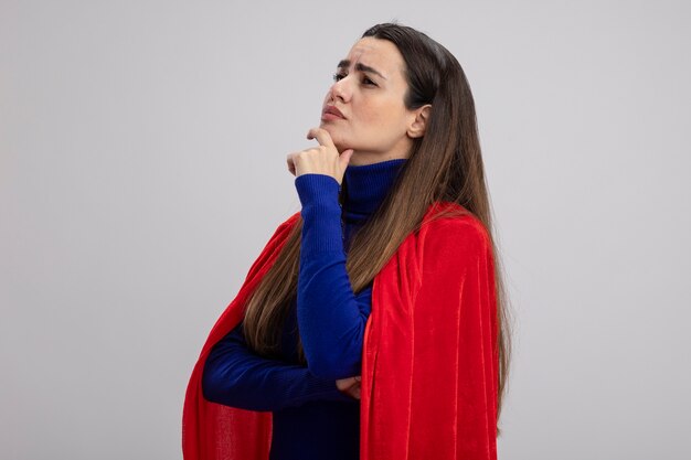 Toughtful joven superhéroe mirando a un lado agarró la barbilla aislado en blanco