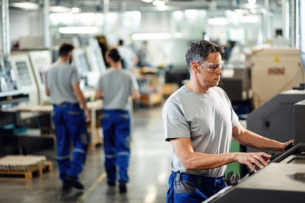 Trabajador adulto medio que opera una máquina CNC mientras trabaja en una instalación industrial