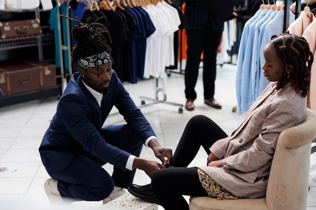 Foto gratuita trabajador afroamericano ayudando al cliente con zapatos elegantes, mujer comprando ropa formal en la sala de exposición. cliente de moda comprando una colección de moda en una boutique. concepto de moda