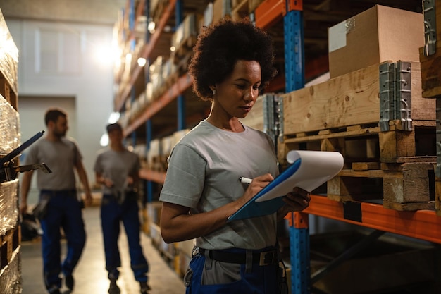 Trabajador afroamericano tomando notas mientras programa el envío en un almacén
