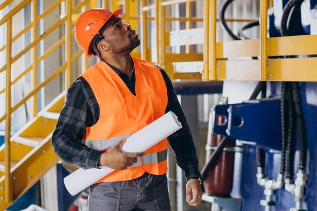 Trabajador afroamericano de uniforme con un sombrero de seguridad en una fábrica.