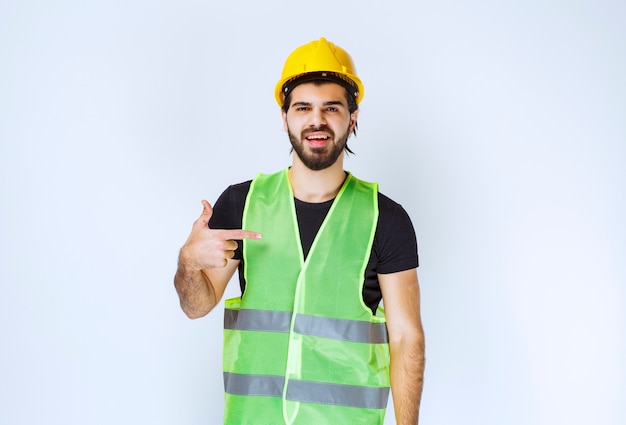 Foto gratuita trabajador en casco amarillo apuntando a sí mismo.