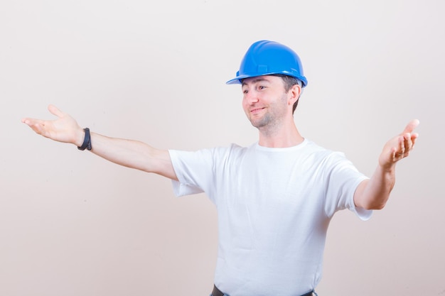 Trabajador de la construcción abriendo los brazos para abrazar en camiseta, casco y mirando amable