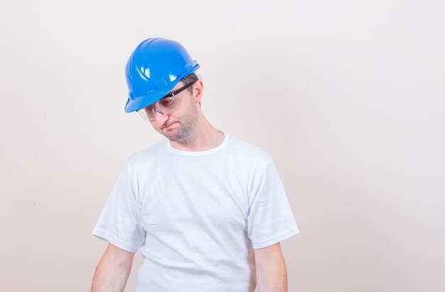 Trabajador de la construcción en camiseta, casco mirando hacia abajo y mirando desesperado