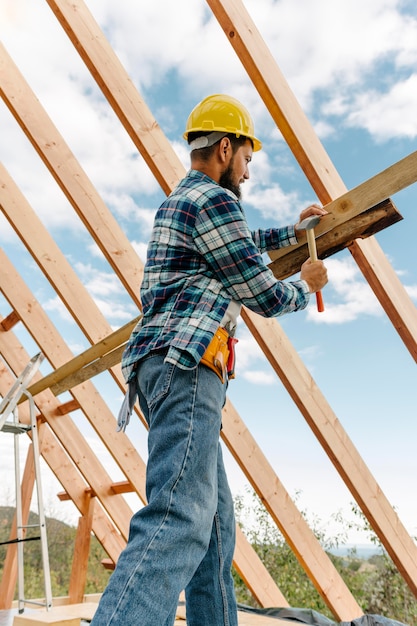 Trabajador de la construcción con casco construyendo el techo de la casa