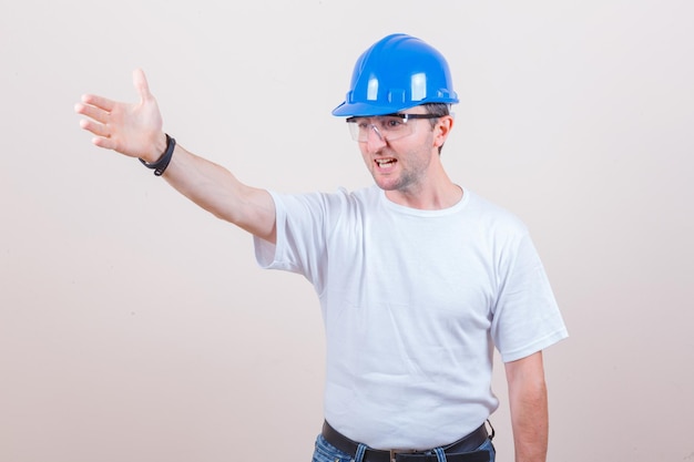 Trabajador de la construcción dando instrucciones en camiseta, jeans, casco y luciendo agresivo