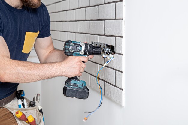 Un trabajador de la construcción electricista con un mono con un taladro durante la instalación de enchufes. Concepto de renovación del hogar.