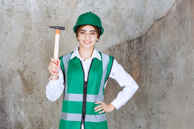 Trabajador de la construcción femenina en casco verde posando con martillo