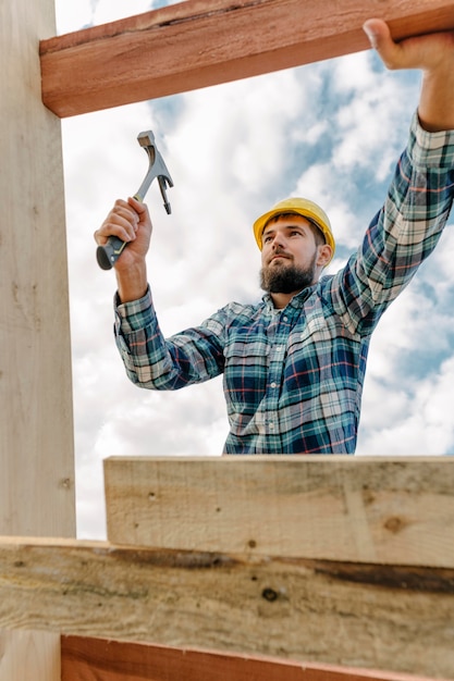 Trabajador de la construcción con martillo y casco construyendo el techo de la casa