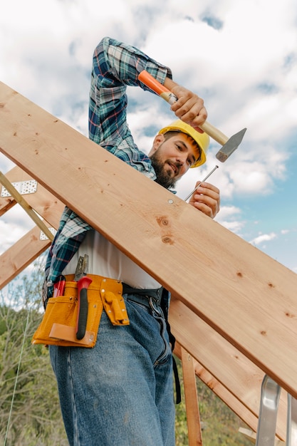 Trabajador de la construcción con martillo construyendo el techo de la casa