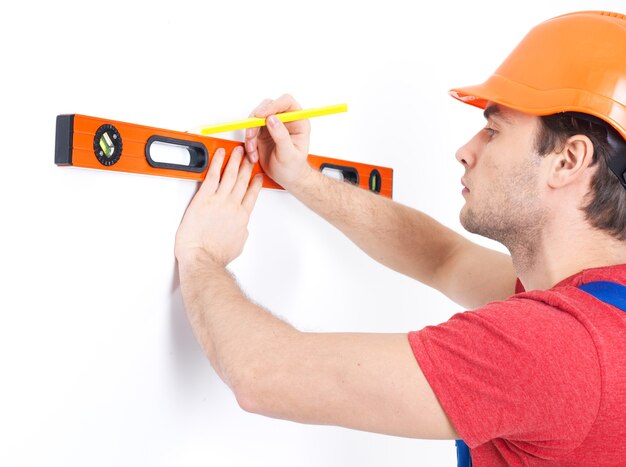 Trabajador de la construcción midiendo con nivel en la pared en blanco